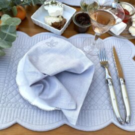 Handgefertigte Serviette mit Fleur de Lys aus hellgrauem Leinen von Atelier Luhabru, ton in ton bestickt, gefaltet auf weißem Teller
