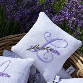 Lavendelkissen mit Monogramm L aus weißem Leinen, lila Initiale mit Lavendelzweig, vor blühendem Lavendel