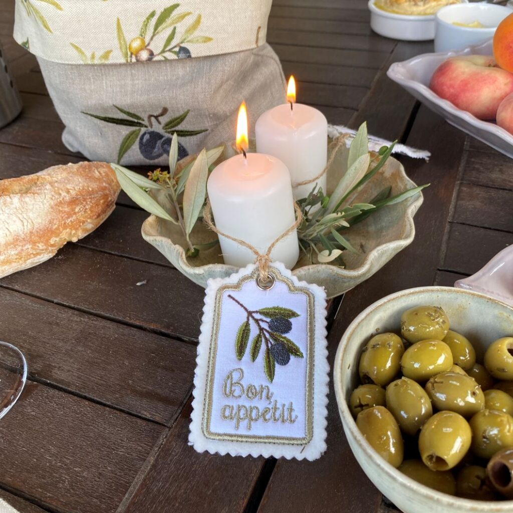 Geschenkanhänger mit Olivenmotiv und Bon Appétit an einer Tischdekoration mit Kerzen und grünen Zweigen